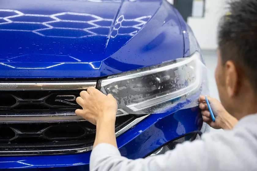 青い車のヘッドライトに保護フィルムを貼る作業の様子