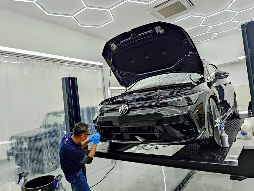 整備工場で黒い車がメンテナンスを受けている様子